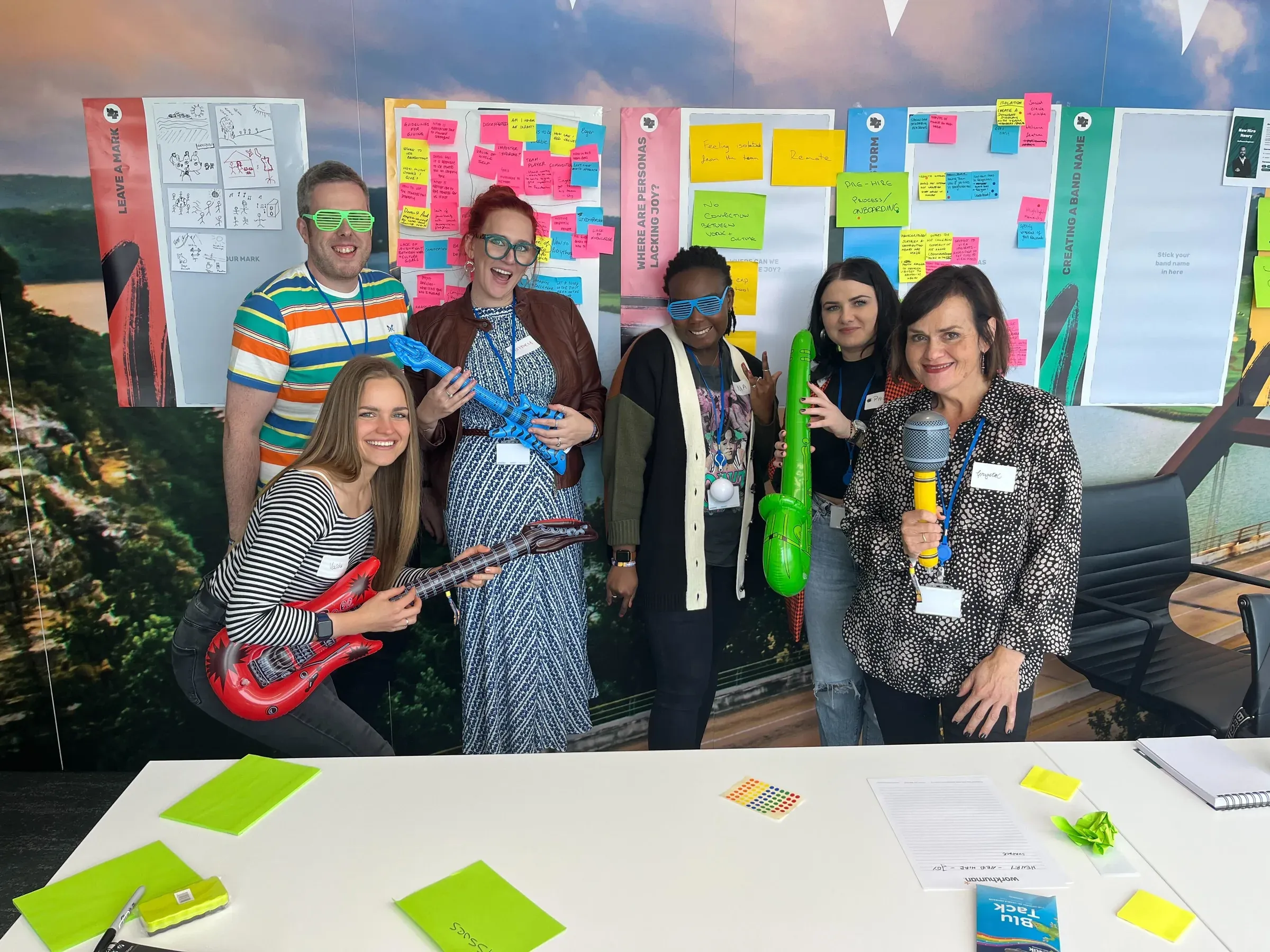 Five people posing with inflatable guitars in front of walls of sticky notes