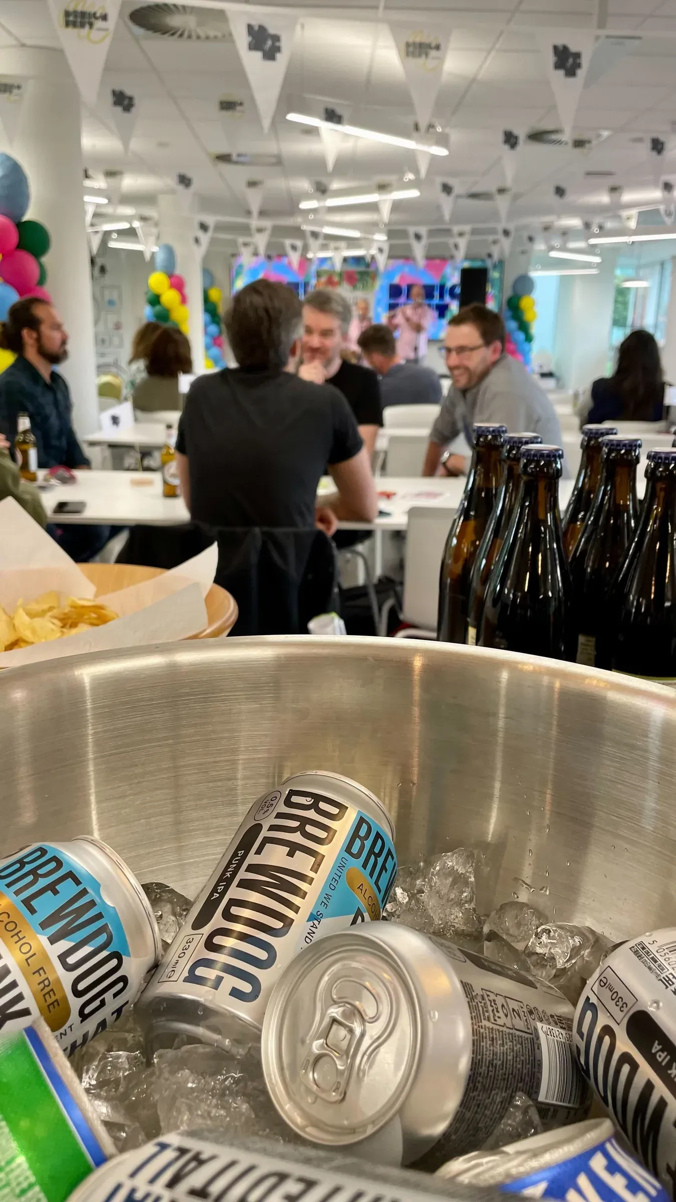 A bucket of cold drinks with people talking in the background