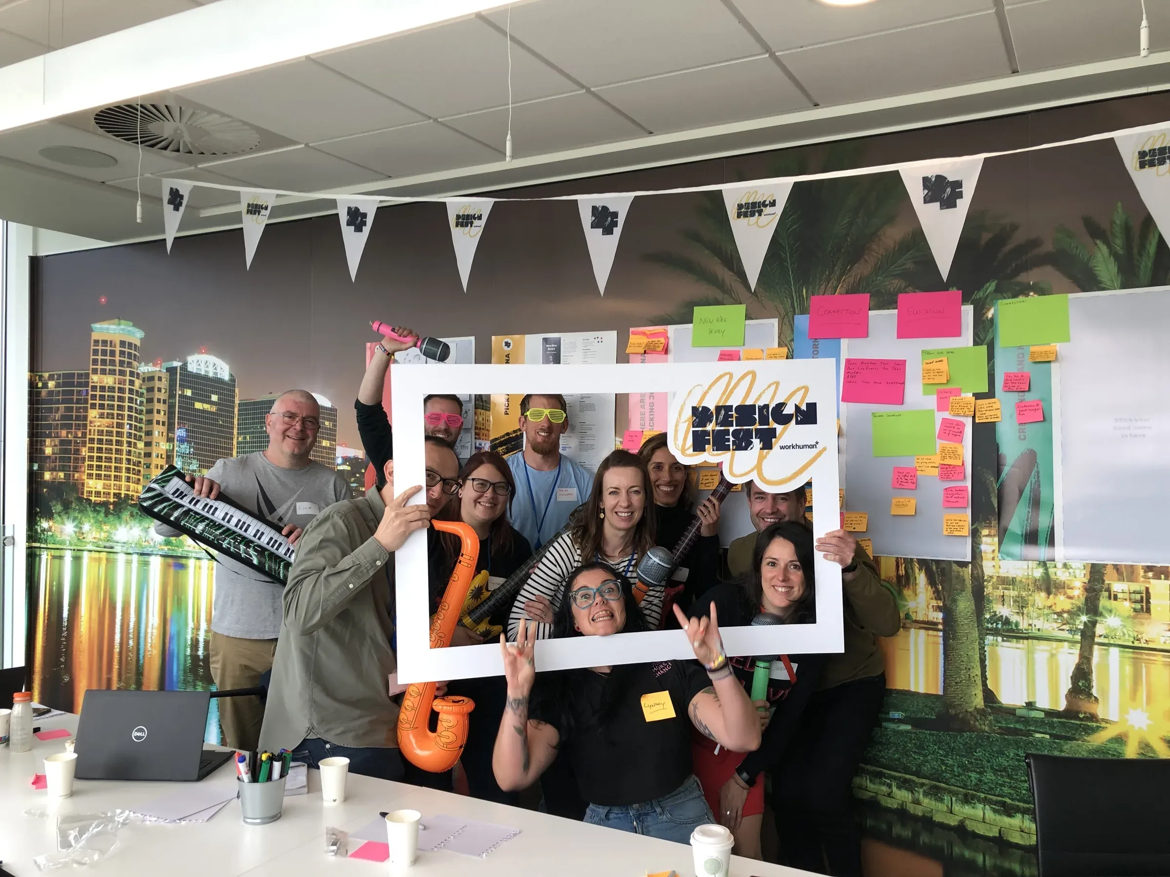 A group of colleagues posing with inflatable instruments inside a large Design Fest picture frame