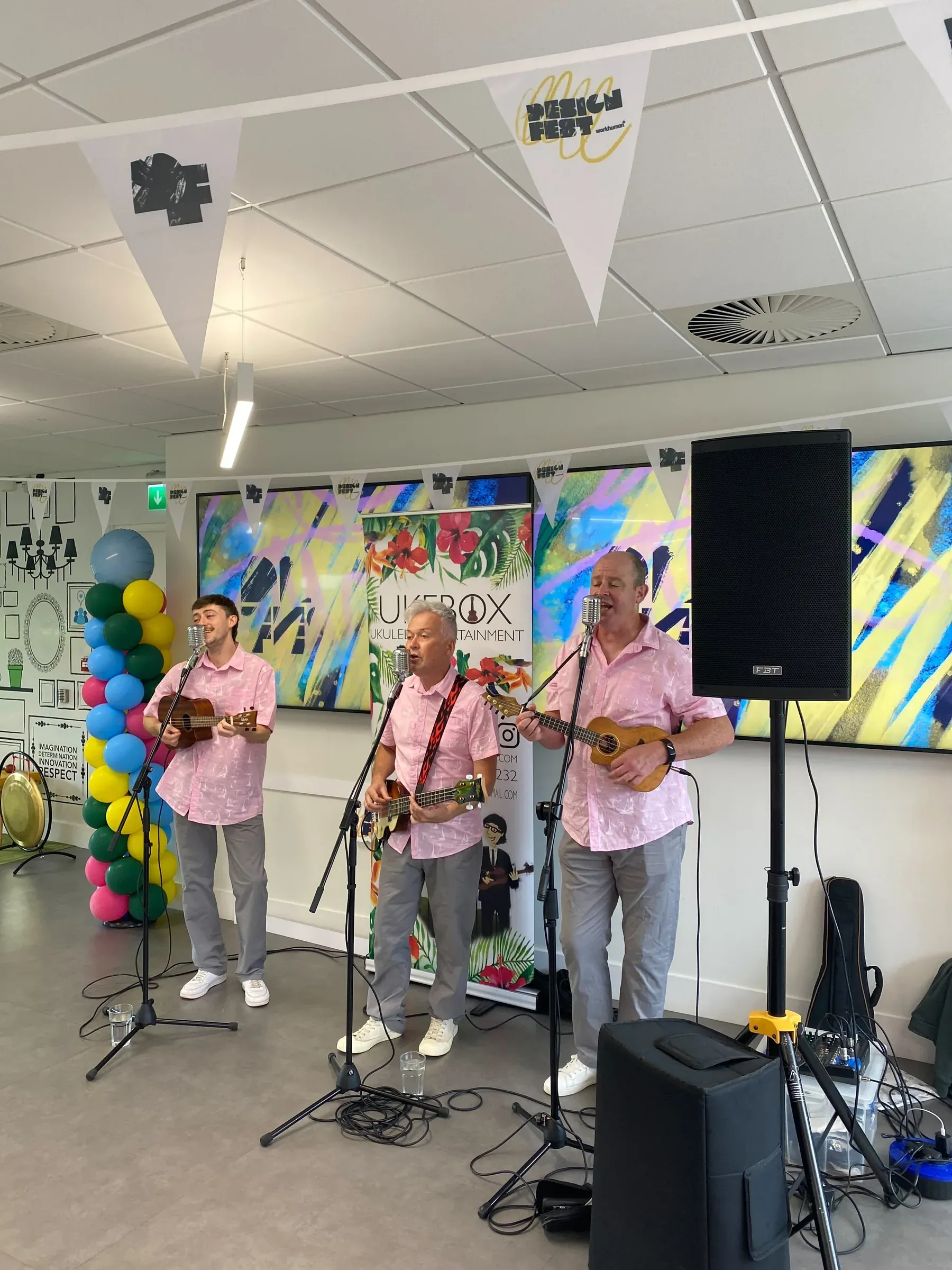 Three musicians playing ukuleles under Design Fest bunting